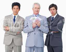 Senior businessman with money standing between his employees