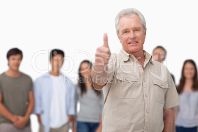 Mature man giving thumb up with young people behind him