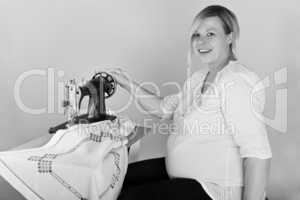 Hochschwangere Frau sitzt an der Naehmaschine
