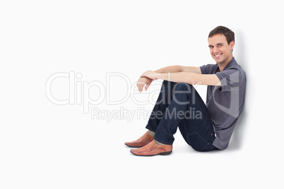 Man smiling while sitting against a wall