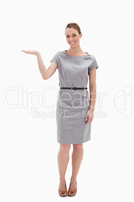 Smiling woman in a dress presenting something with her hand