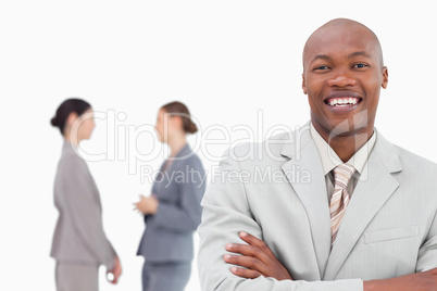 Smiling businessman with folded arms and co-workers behind him