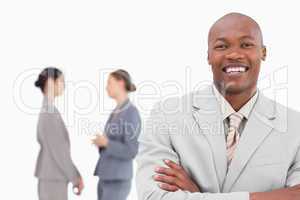 Smiling businessman with folded arms and co-workers behind him