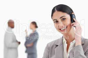 Smiling businesswoman with cellphone and co-workers behind her