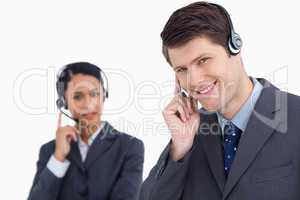 Close up of smiling call center agent with co-worker behind him