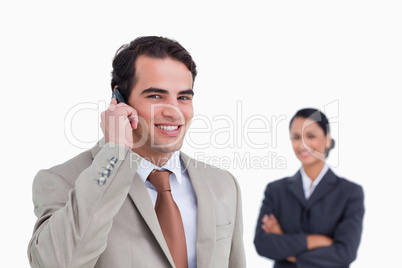 Smiling salesman on his cellphone with colleague behind him