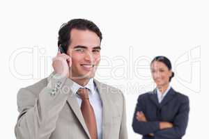 Smiling salesman on his cellphone with colleague behind him