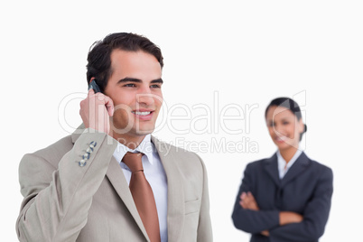 Smiling salesman on his mobile phone with colleague behind him