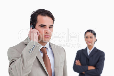 Serious salesman on his cellphone with colleague behind him