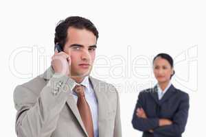 Serious salesman on his cellphone with colleague behind him