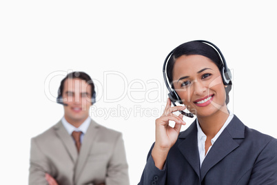 Smiling telephone support employee with co-worker behind her