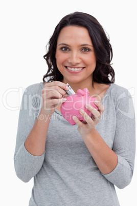 Smiling woman putting money into her piggy bank