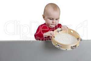 young child holding tambourine behind grey shield