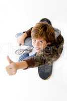 top view of boy sitting on skate and showing thumbs up