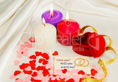 Two rings and a card with marriage proposal with three candles