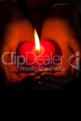 Human hands hold heart shaped burning candle