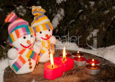 Two snowmen with two burning heart shaped candles