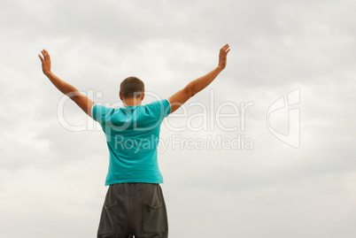 Young man staying with raised hands against blue sky