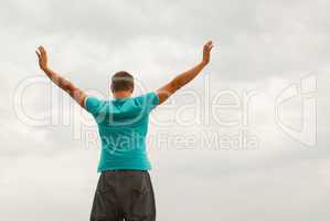 Young man staying with raised hands against blue sky