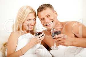 Couple lying in bed together sharing wine