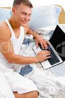high angle view of smiling man working on laptop in bed