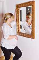 Hochschwangere Frau betrachtet sich im Spiegel