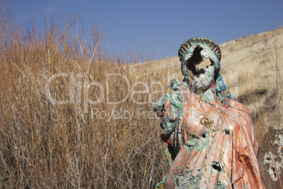 A grungy religious statue in teh middle of nowhere.