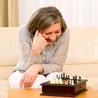 Senior woman play chess happy sit on sofa
