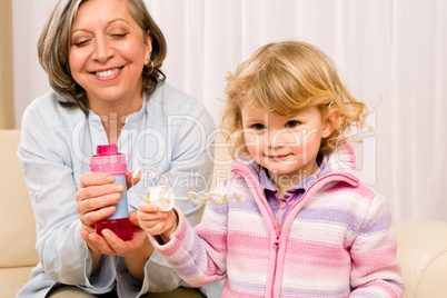 Little girl with grandmother play bubble blower