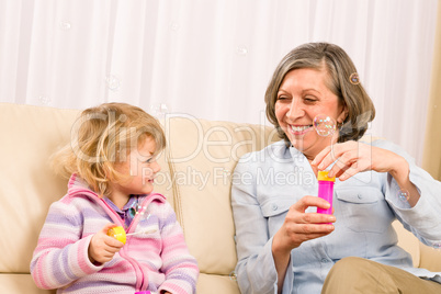 Little girl with grandmother play bubble blower