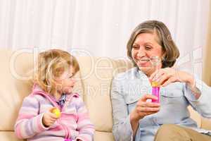 Little girl with grandmother play bubble blower