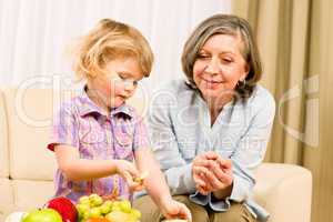Grandmother with granddaughter eat fruit at home