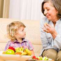 Little girl watch grandmother eat fruit