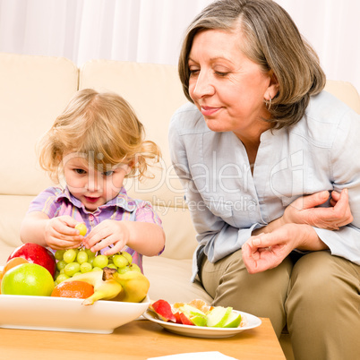 Grandmother with granddaughter eat fruit at home