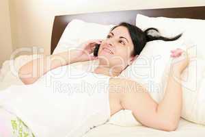 Happy young woman in bed on cellphone