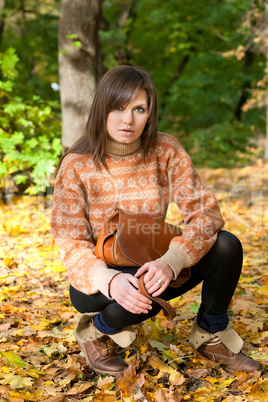 Young girl with handbag sitting in the forest