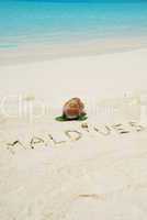 Maldives written in a sandy tropical beach and coconut fruit