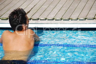 Young man relaxing at the edge of the swimming pool