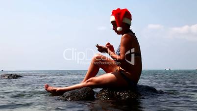 Woman on the beach in santa hat calls on the phone.