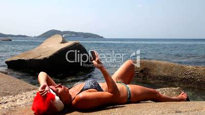 Woman on the beach in santa hat calls on the phone