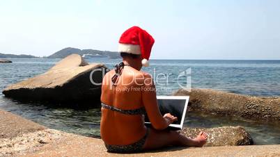 Woman on the beach in santa hat with a laptop.