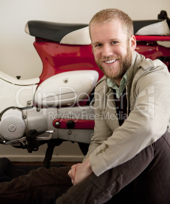 Man is sitting next to the red and white bike scooter.