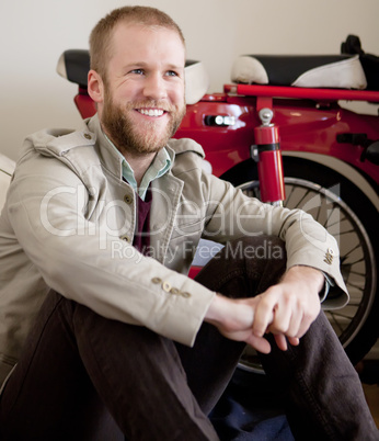 Young man with bear sitting next to bike scooter.