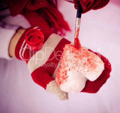 Red gloves painting snow heart in red.