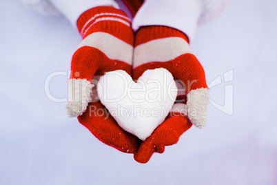 Red gloves hold white snow heart.