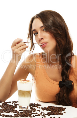 junge frau sitzt an einem tisch mit einem glas latte macchiato kaffee mit löffel im mund