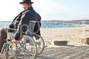 Mann sitzt im Rollstuhl am Strand