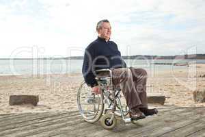 Mann sitzt im Rollstuhl am Strand