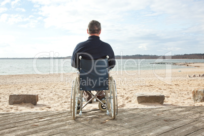 Mann sitzt im Rollstuhl am Strand