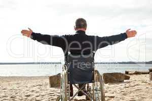 Mann sitzt im Rollstuhl am Strand